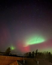 Nordlichter leuchten in lebhaften Grün- und Rottönen über einem verschneiten Feld, während der Nachthimmel mit Sternen übersät ist.