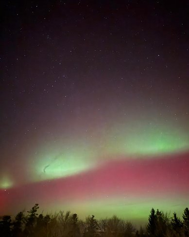 Nordlichter leuchten in lebhaften Grün- und Rottönen über einem verschneiten Feld, während der Nachthimmel mit Sternen übersät ist.