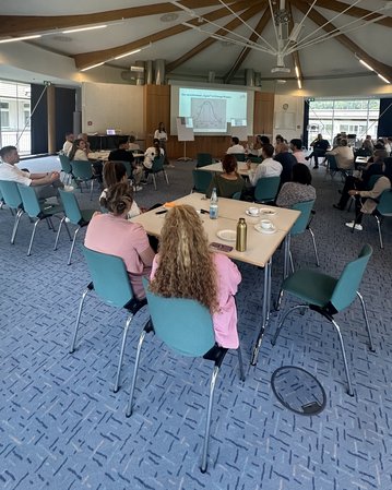 Eine Gruppe von Menschen sitzt in einem Konferenzraum, während eine Präsentation zu Changemanagement an einer Leinwand gezeigt wird.