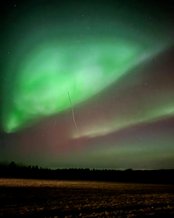 Nordlichter leuchten in lebhaften Grün- und Rottönen über einem verschneiten Feld, während der Nachthimmel mit Sternen übersät ist.