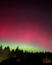 Nordlichter leuchten in lebhaften Grün- und Rottönen über einem verschneiten Feld, während der Nachthimmel mit Sternen übersät ist.