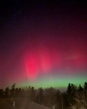 Nordlichter leuchten in lebhaften Grün- und Rottönen über einem verschneiten Feld, während der Nachthimmel mit Sternen übersät ist.