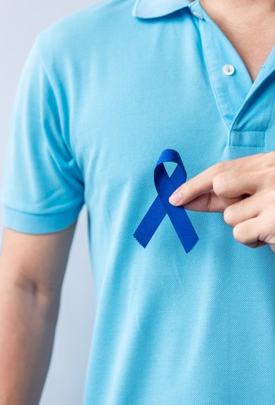 Eine Person in einem blauen Polohemd zeigt auf eine blaue Schleife, die auf der Brust befestigt ist.