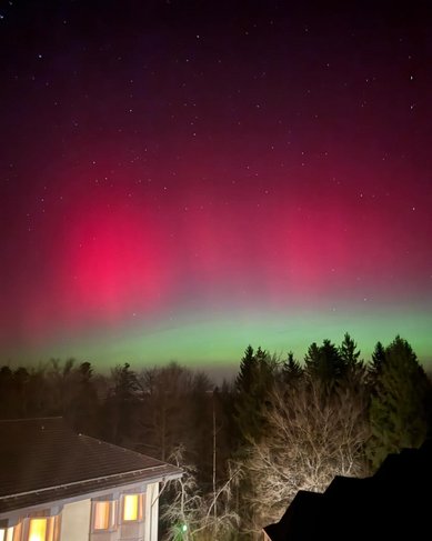 Nordlichter leuchten in lebhaften Grün- und Rottönen über einem verschneiten Feld, während der Nachthimmel mit Sternen übersät ist.